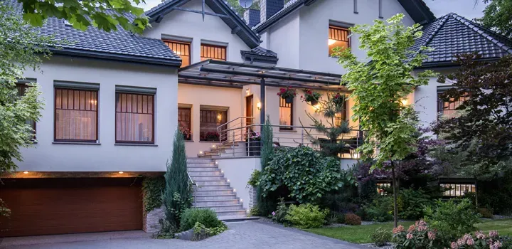 A two-story home with a lit porch and landscaped yard at dusk